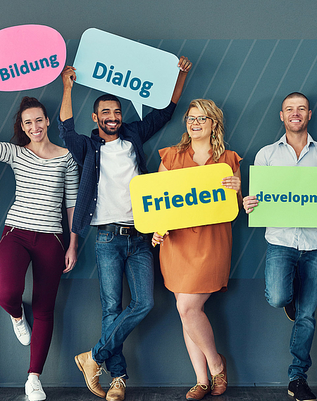 Im Dienst von Frieden, Demokratie und Entwicklung Sechs Personen stehen nebeneinander und halten Schilder hoch mit den Aufschriften "Demokratie", "Bildung", "Dialog", "Frieden", "Development" und "Entwicklung"