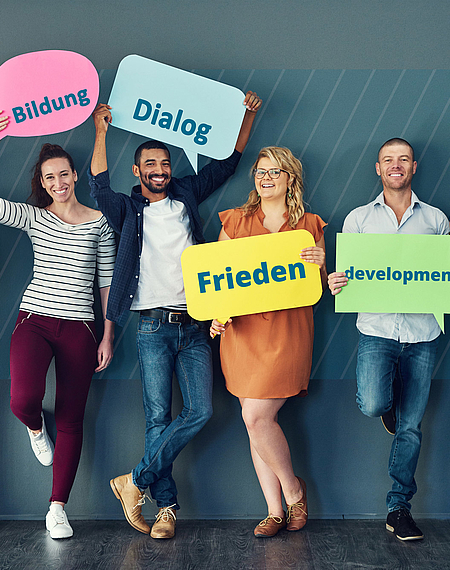 Im Dienst von Frieden, Demokratie und Entwicklung Sechs Personen stehen nebeneinander und halten Schilder hoch mit den Aufschriften "Demokratie", "Bildung", "Dialog", "Frieden", "Development" und "Entwicklung"